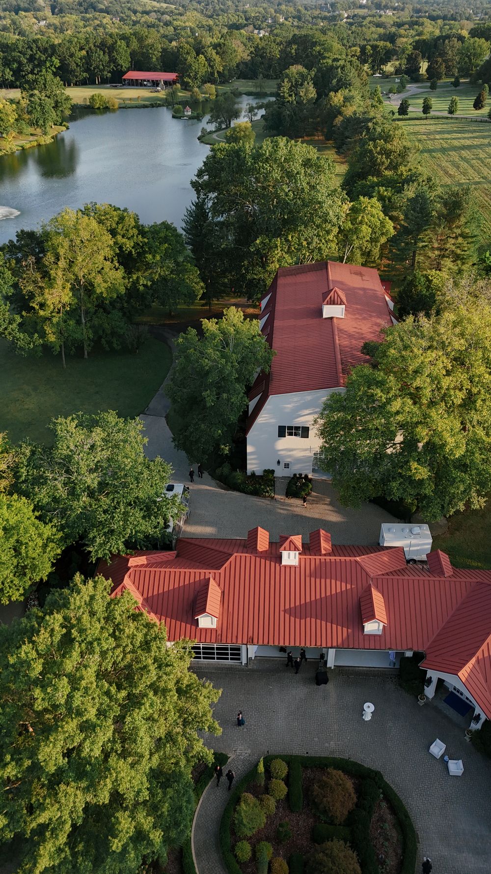 Aerial view of a sprawling estate with red-roofed buildings surrounded by lush greenery and a lake.