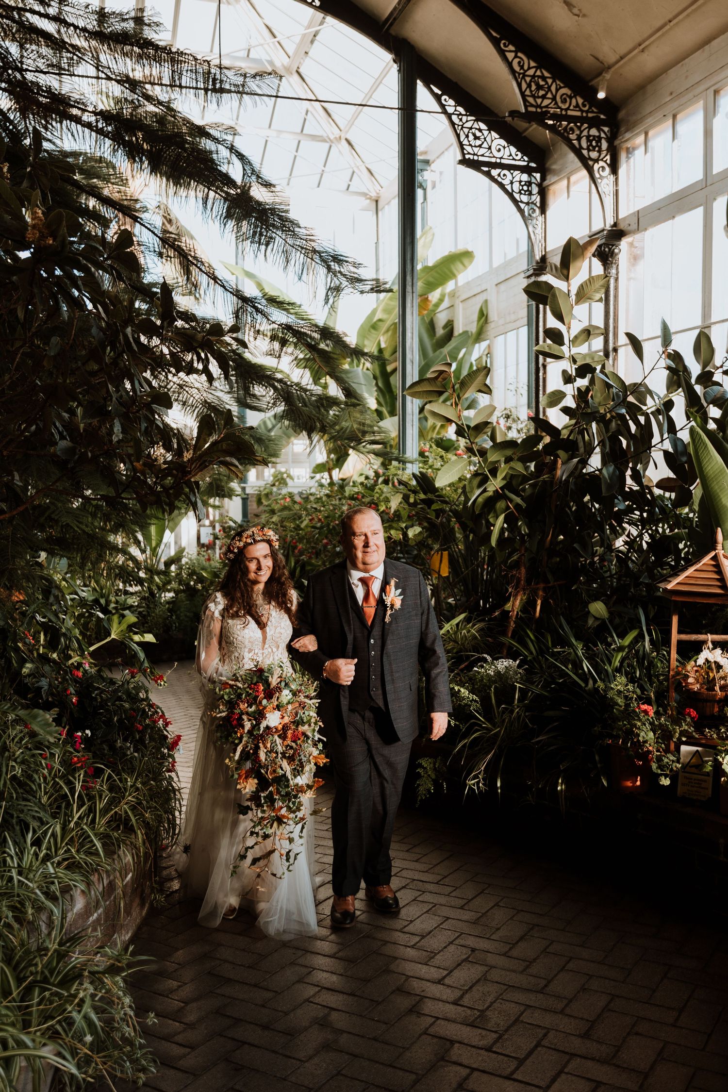 Wedding ceremony taking place in a lush greenhouse conservatory with tropical plants and natural lighting.