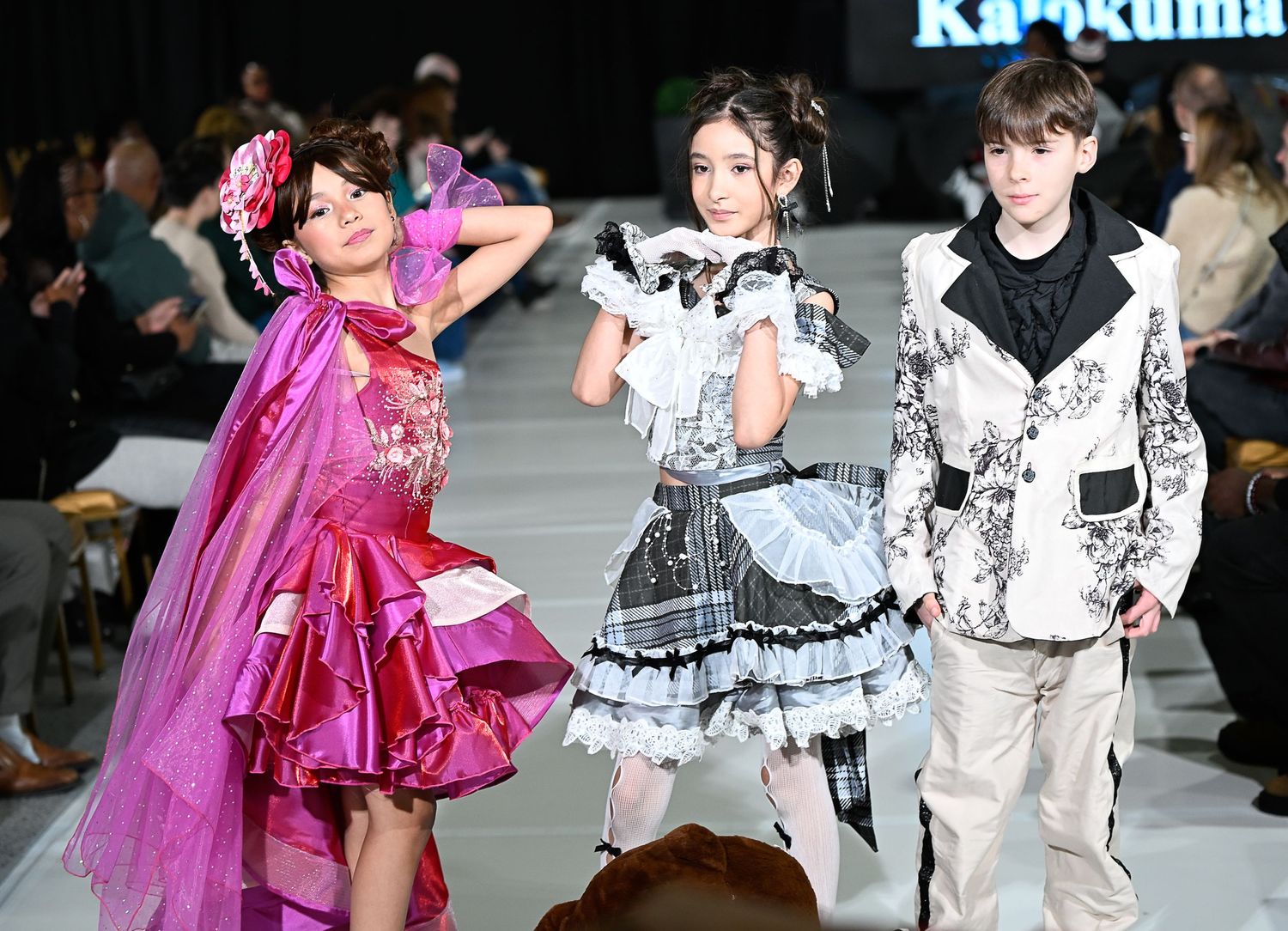Models showcase a mix of frilly gothic lolita and bright pink fashion designs on a runway during a fashion show.
