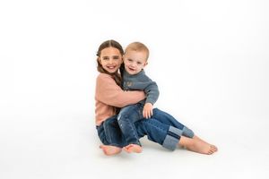 Two siblings in casual wear posing together on a white background for personality portraits.
