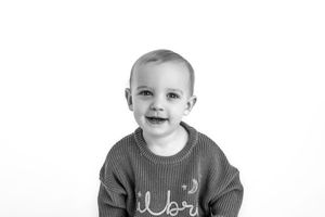 Child wearing a sweater smiling brightly in black and white portrait.
