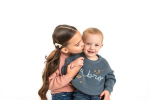 Sweet candid moment between brother and sister captured in studio setting against white background.