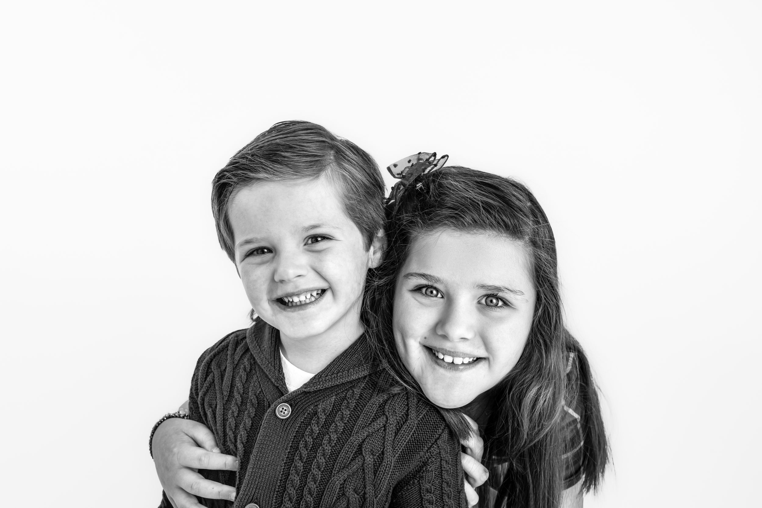 Two children embracing and smiling together in black and white studio portrait.