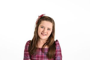 A young student wearing a plaid burgundy shirt smiles warmly against a white background.