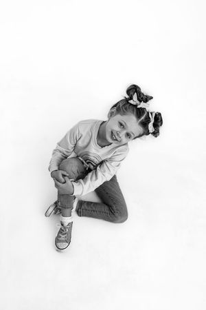 Black and white photo showing child seated on a white studio backdrop.