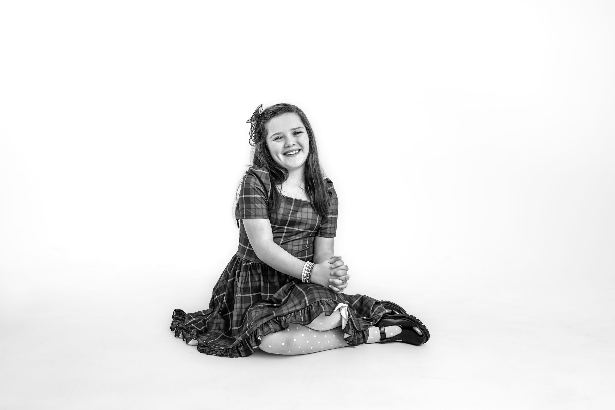 black and white photo of a Girl in a plaid dress relaxing on a white studio background.