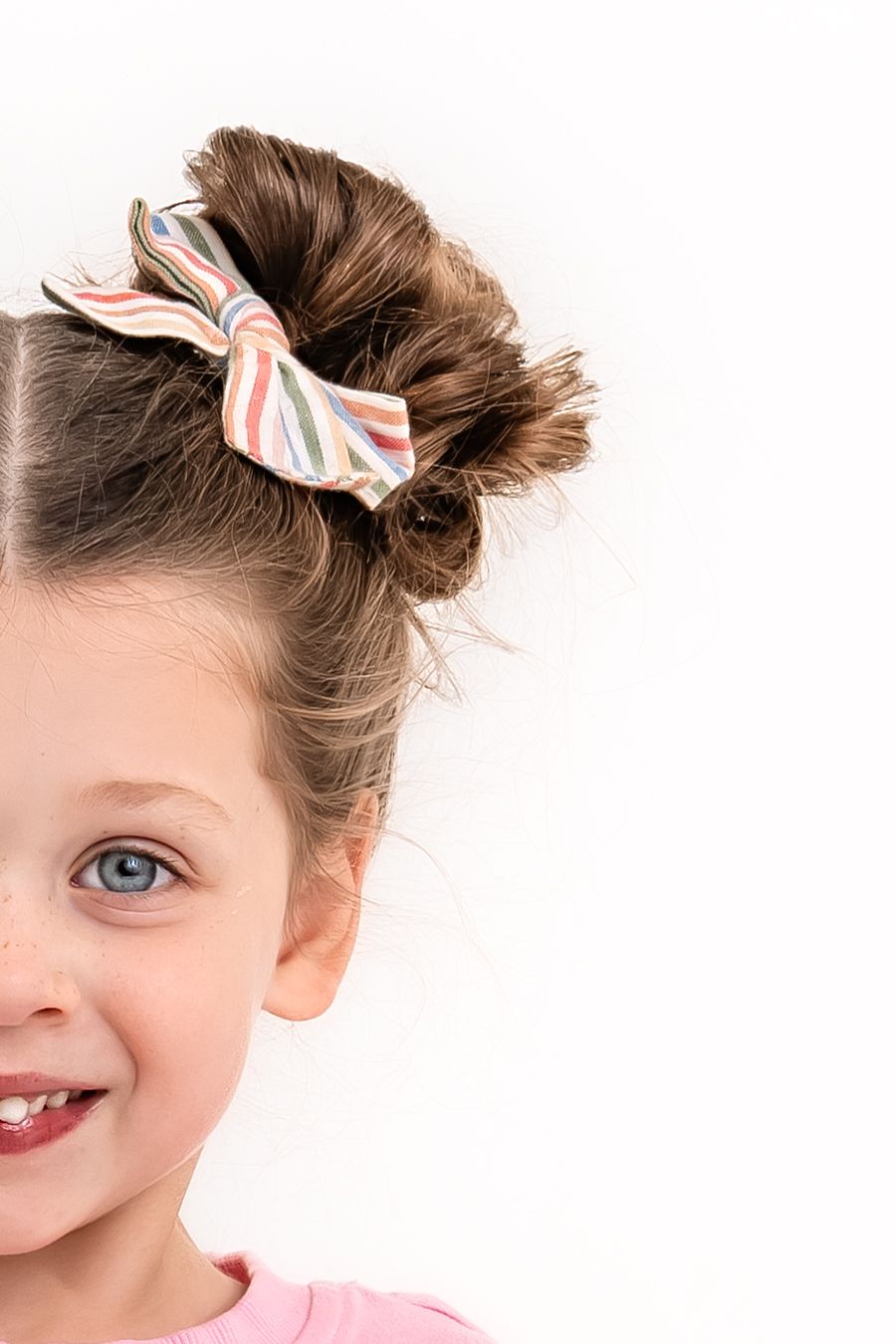 Close up portrait showing half of a girl's smiling face with a pig-tail bun and colorful bow.