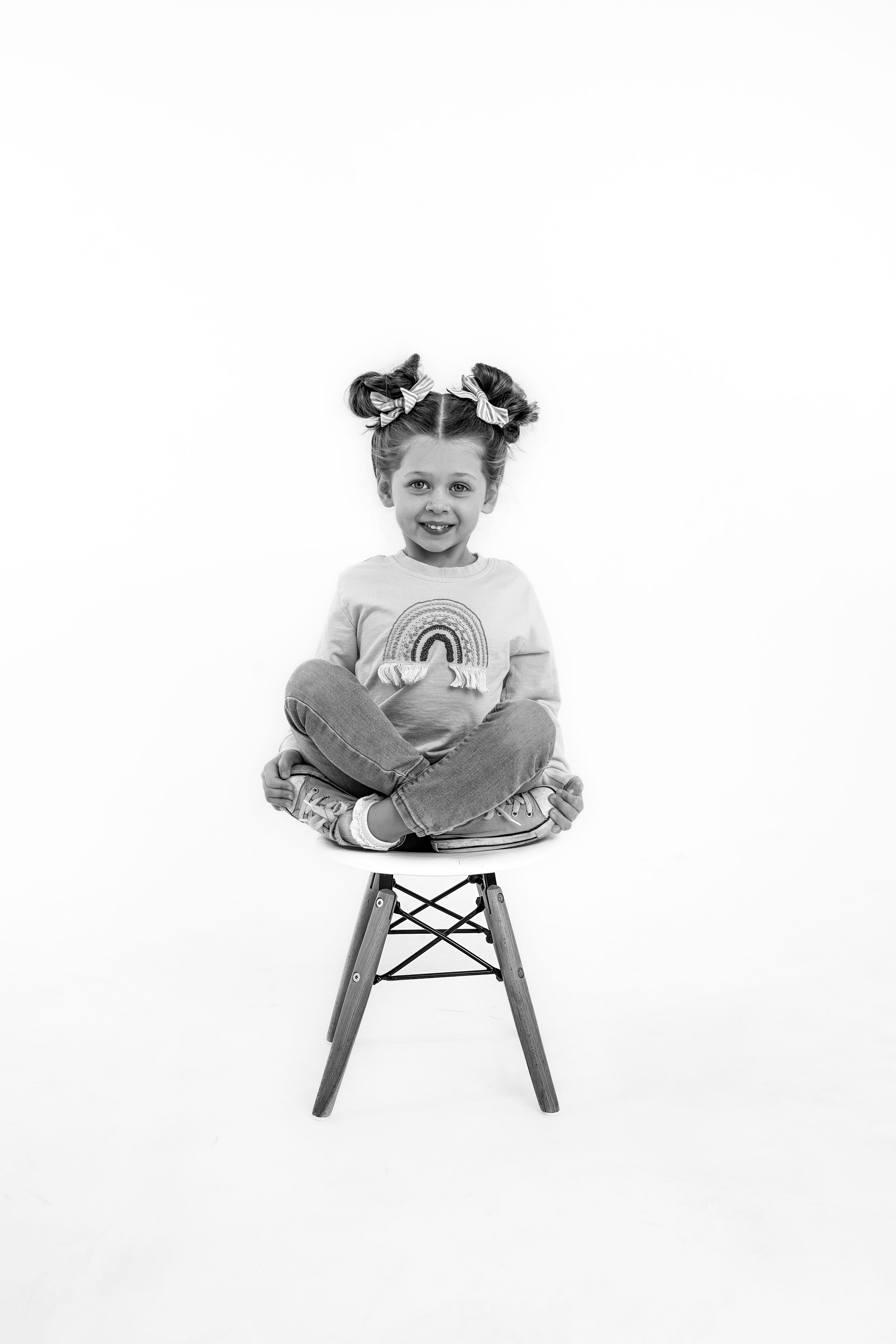 Studio portraits showing a child seated on a modern white chair against a white background.