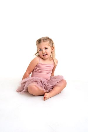 Smiling girl in a pink ballet outfit against a white background in studio.