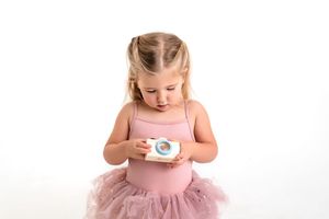 A young child in a pink tutu dress looking down intently at a toy camera in her hands.