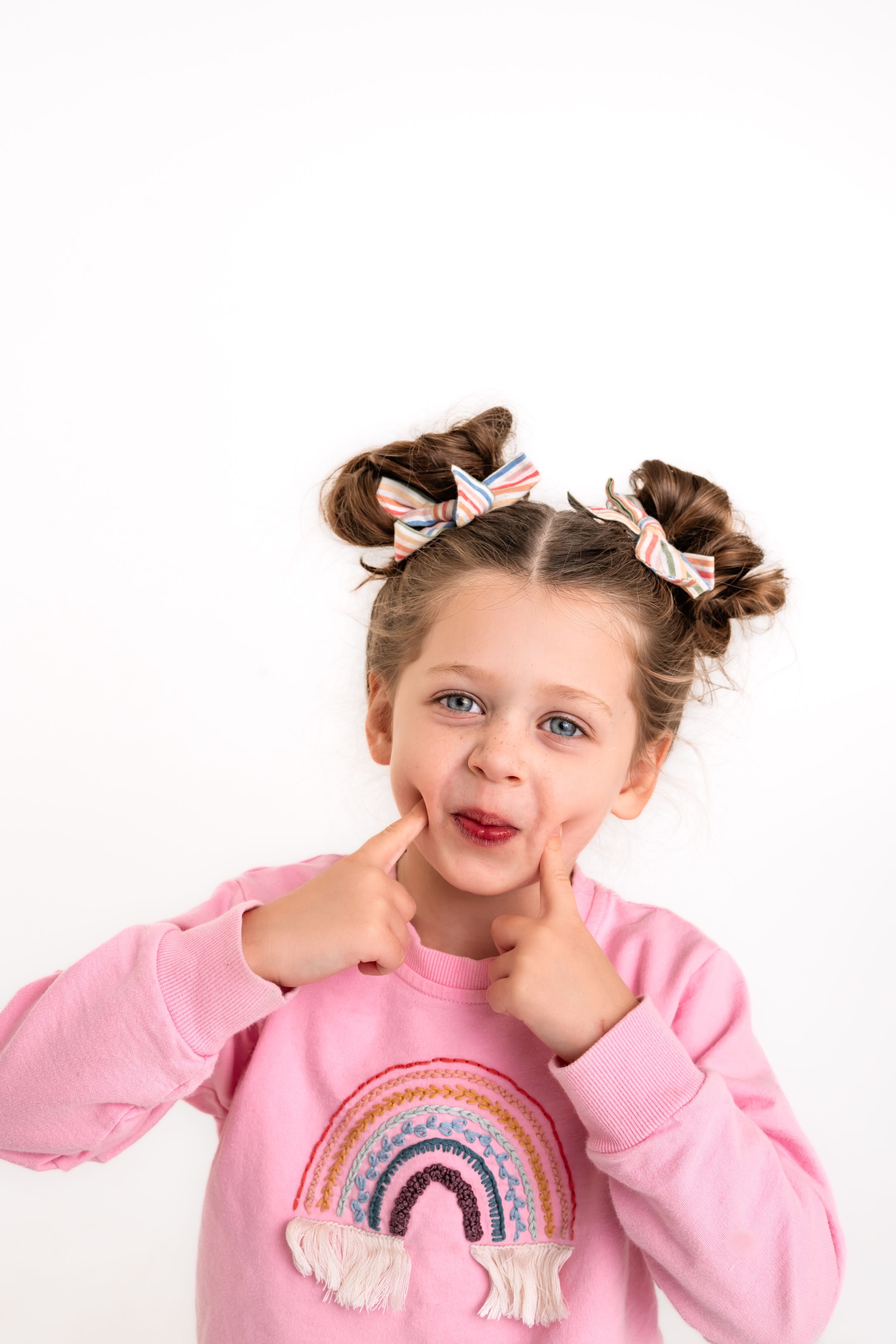 A girl in space buns and bows makes a little face against a white backdrop for white studio portraits.