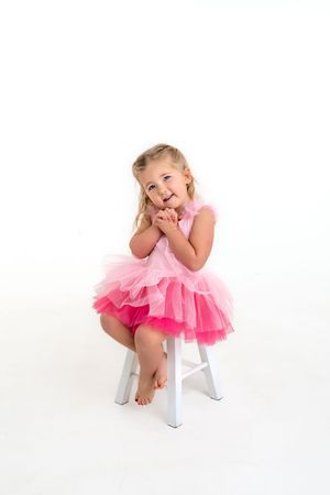 Three playful poses of a young dancer in a pink tulle dress and white stool against a bright white background.