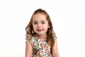 Sweet expressions from young girl while wearing a floral print dress against a white background.