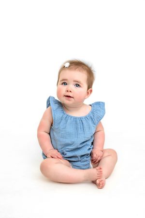 Baby wearing blue ruffled outfit sitting on white background in different poses for personality portrait mini session