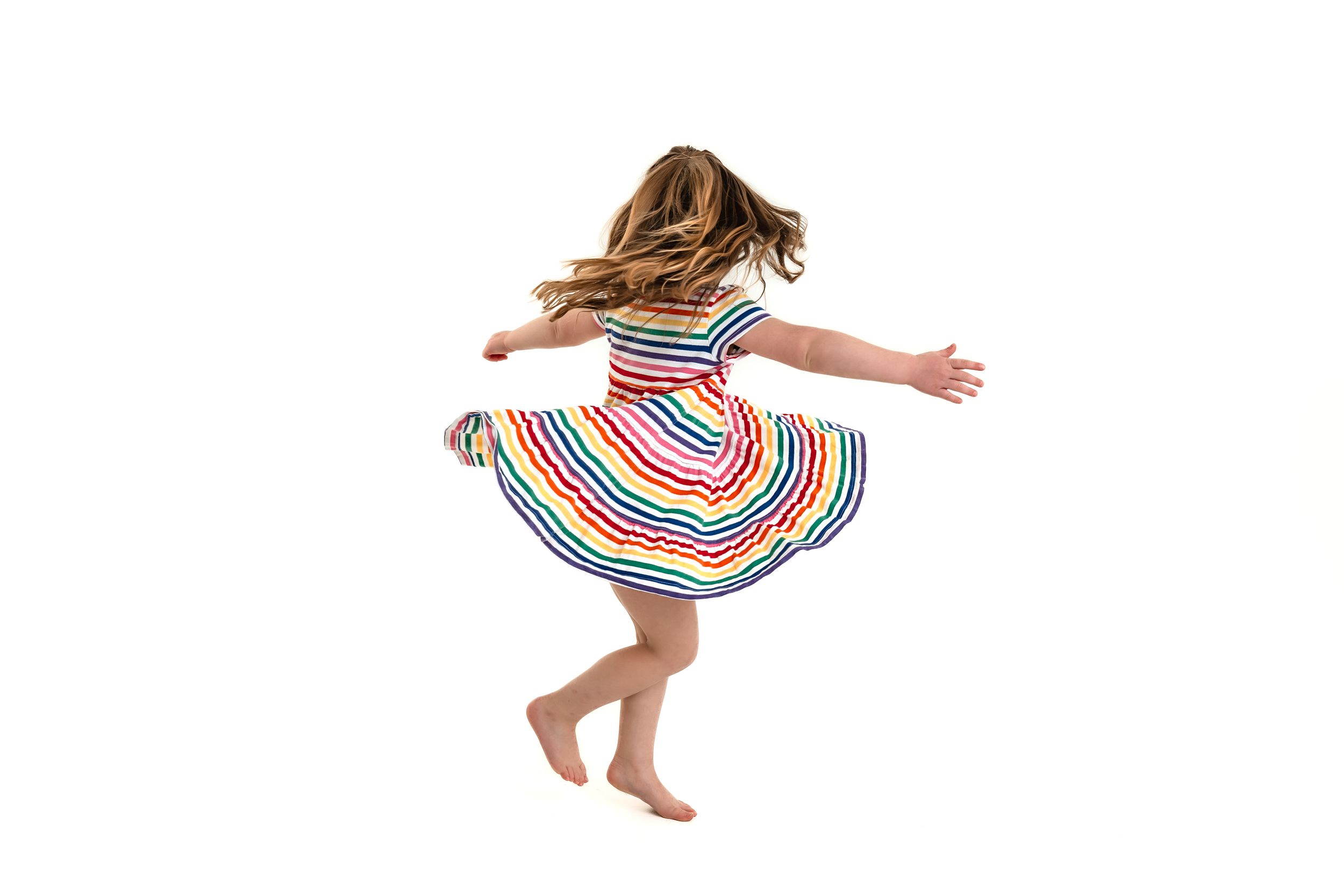 Action shots of someone jumping and twirling in a colorful striped dress against white background for personality portrait mini sessions.