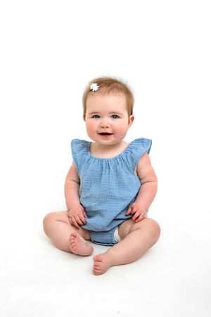 Baby wearing blue sits on white studio background showing happy expressions.