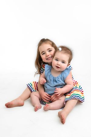Sweet studio portraits showing tender moments between sisters on white background for personality mini sessions.
