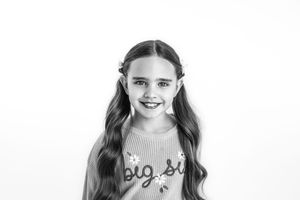 Black and white portrait of a girl in pigtails posing against a clean white studio backdrop.