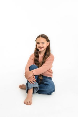 A casual portrait series showing someone in a peach sweater and jeans sitting against a white background.