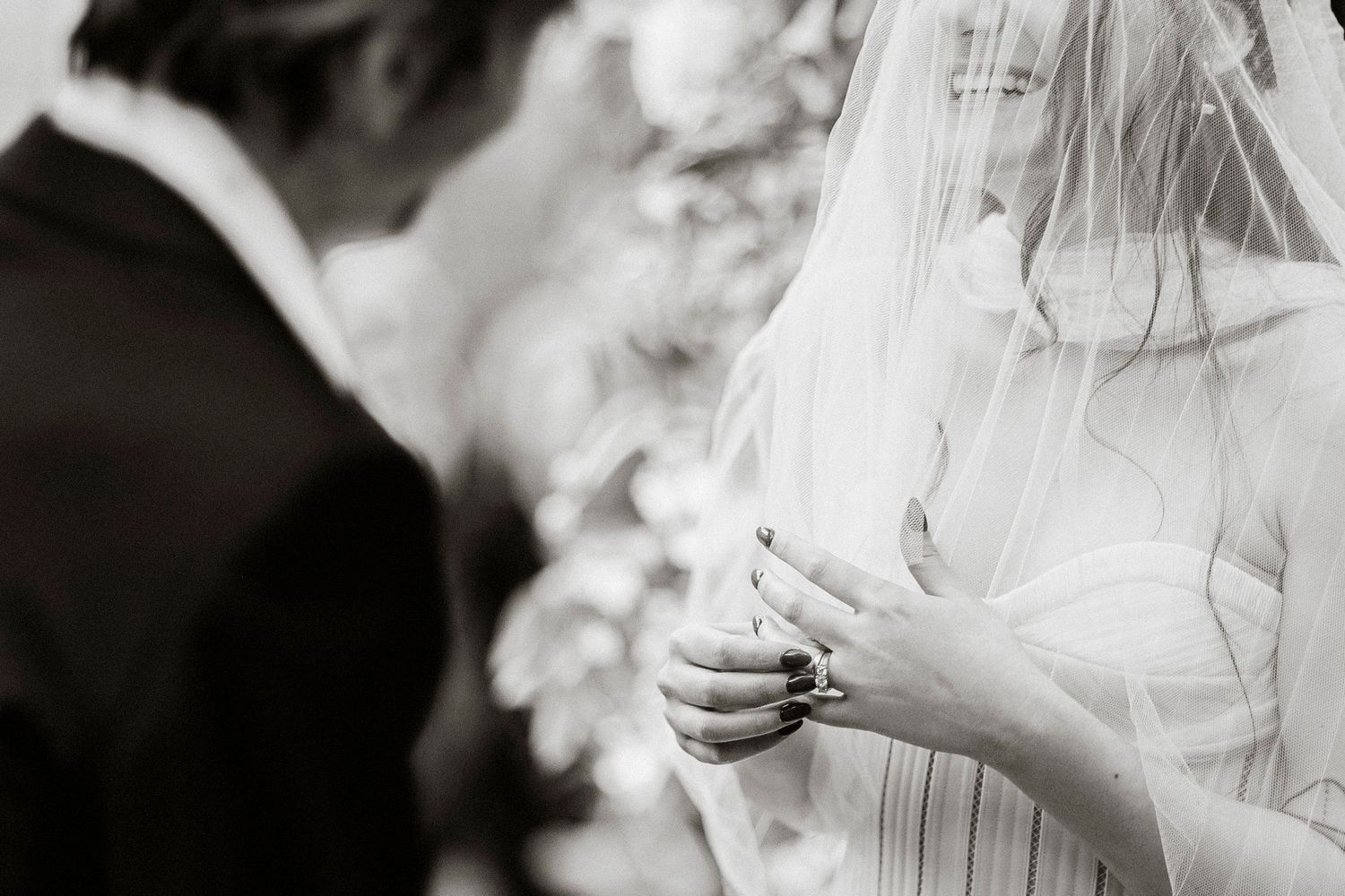 Black and white close-up photo of a bride's hands adjusting her veil during a wedding preparation moment.