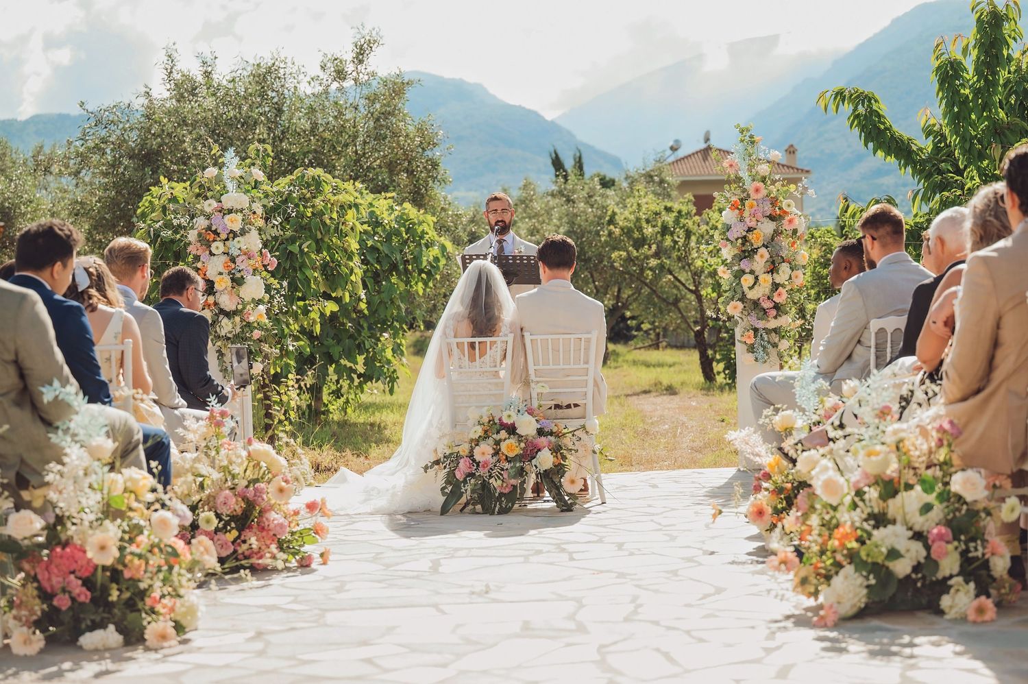 Panoramic view of an outdoor wedding ceremony with mountain backdrop and floral arrangements lining the aisle.