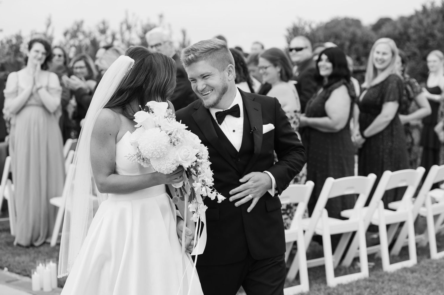 A joyful black and white photo of a wedding ceremony with a newlywed couple walking down the aisle while guests look on.