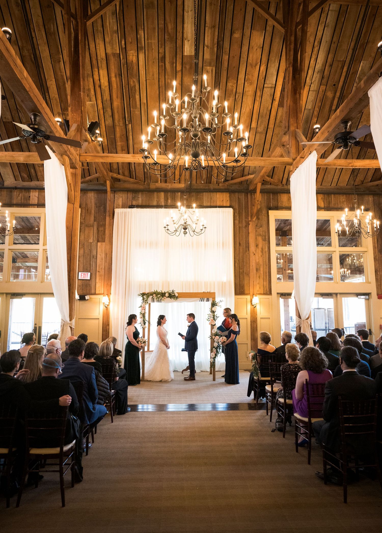 A couple walks hand in hand outside a rustic red barn venue with snow on the ground during a winter wedding celebration.