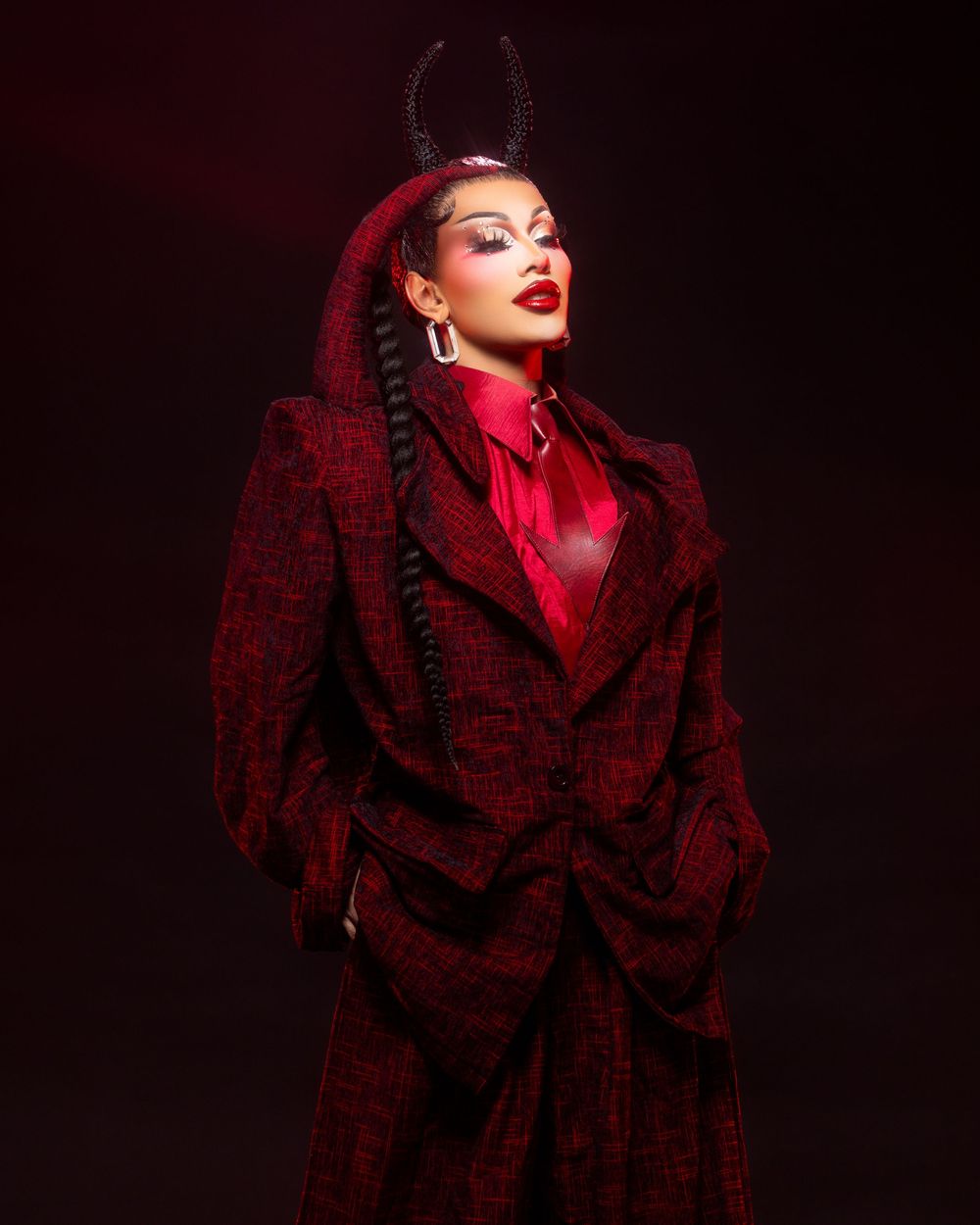 A dramatic fashion portrait shot in red lighting with a dark coat collar against a black background.