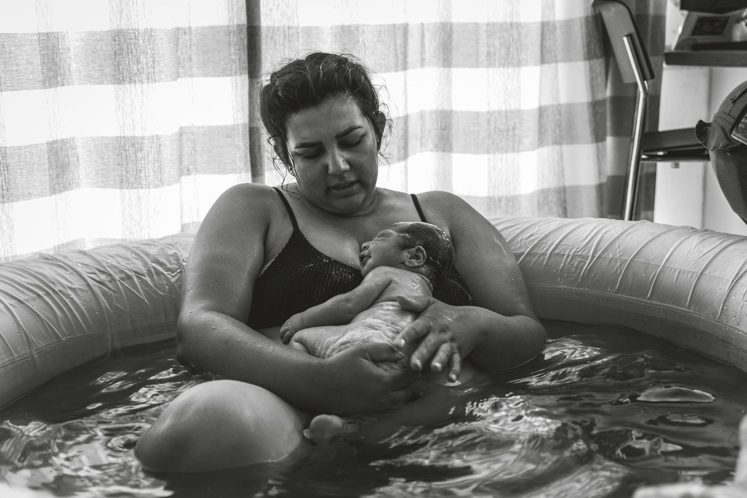 A tender moment captured in black and white as someone rests with a baby on a floral patterned couch.