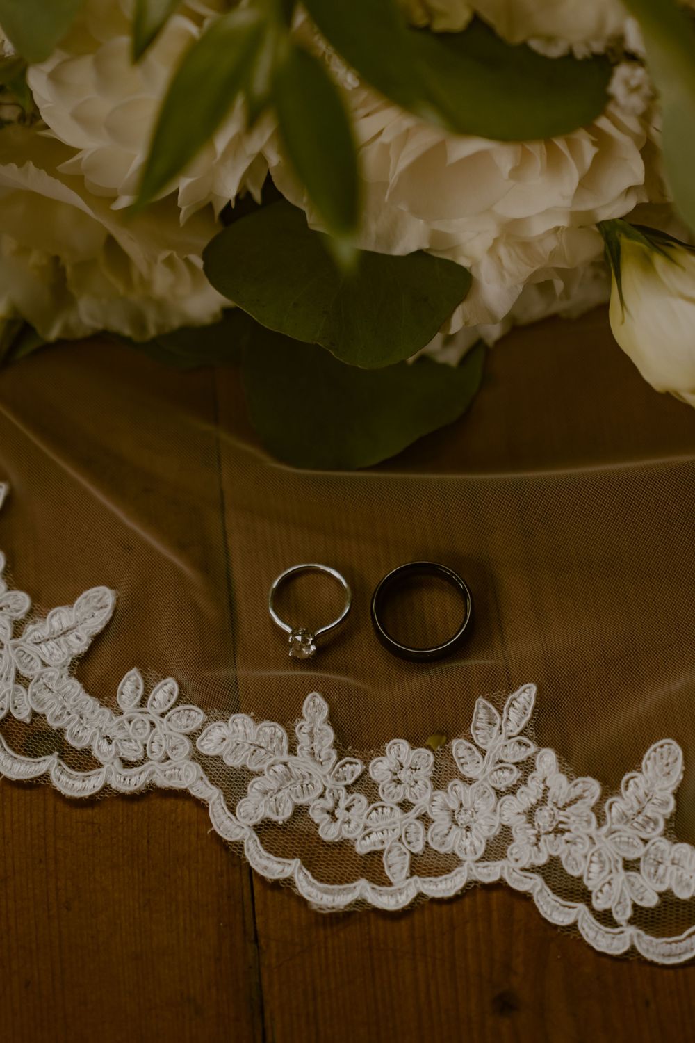 Wedding details featuring delicate white lace trim and wedding rings on wooden surface.