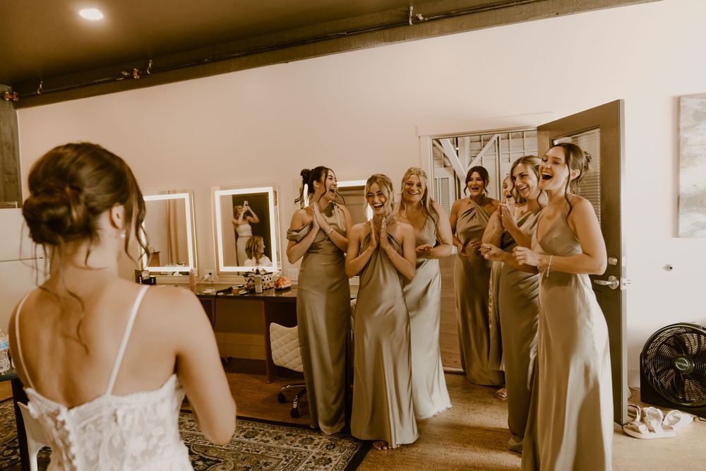 A bride in a white dress shares a special moment with her bridesmaids wearing matching gowns during wedding preparations.