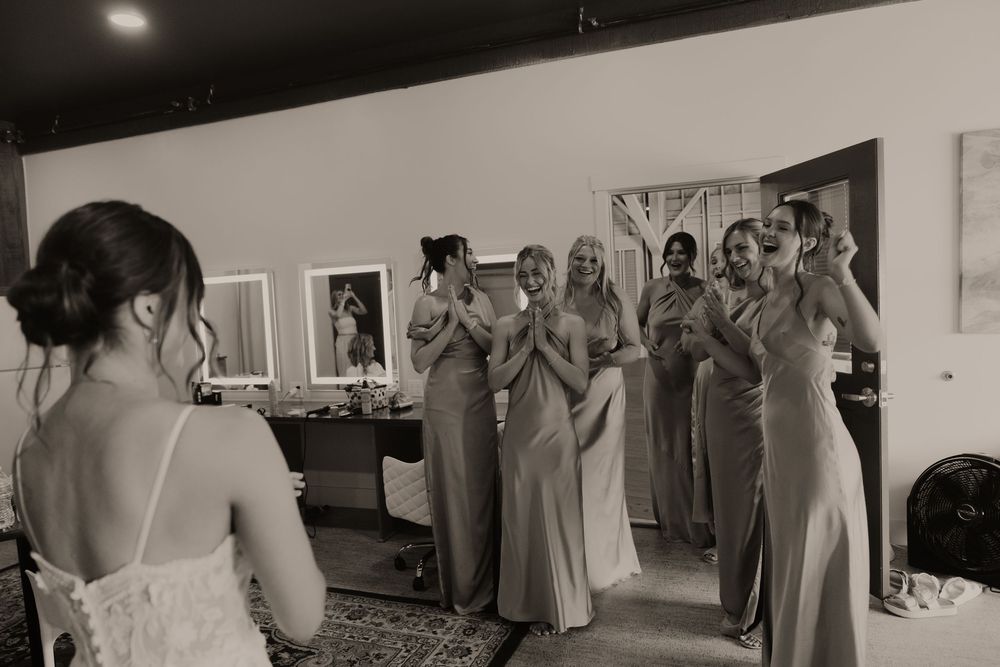 A black and white photo shows a bride and bridesmaids in elegant dresses during an emotional wedding moment.