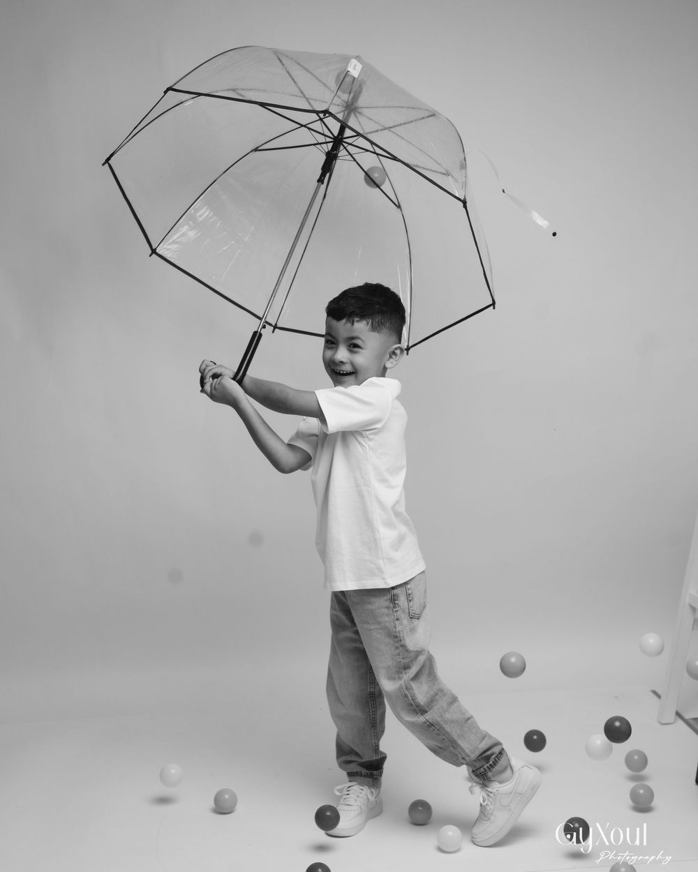 A sequence of black and white photos showing a child in white playing with an umbrella and bouncing balls.
