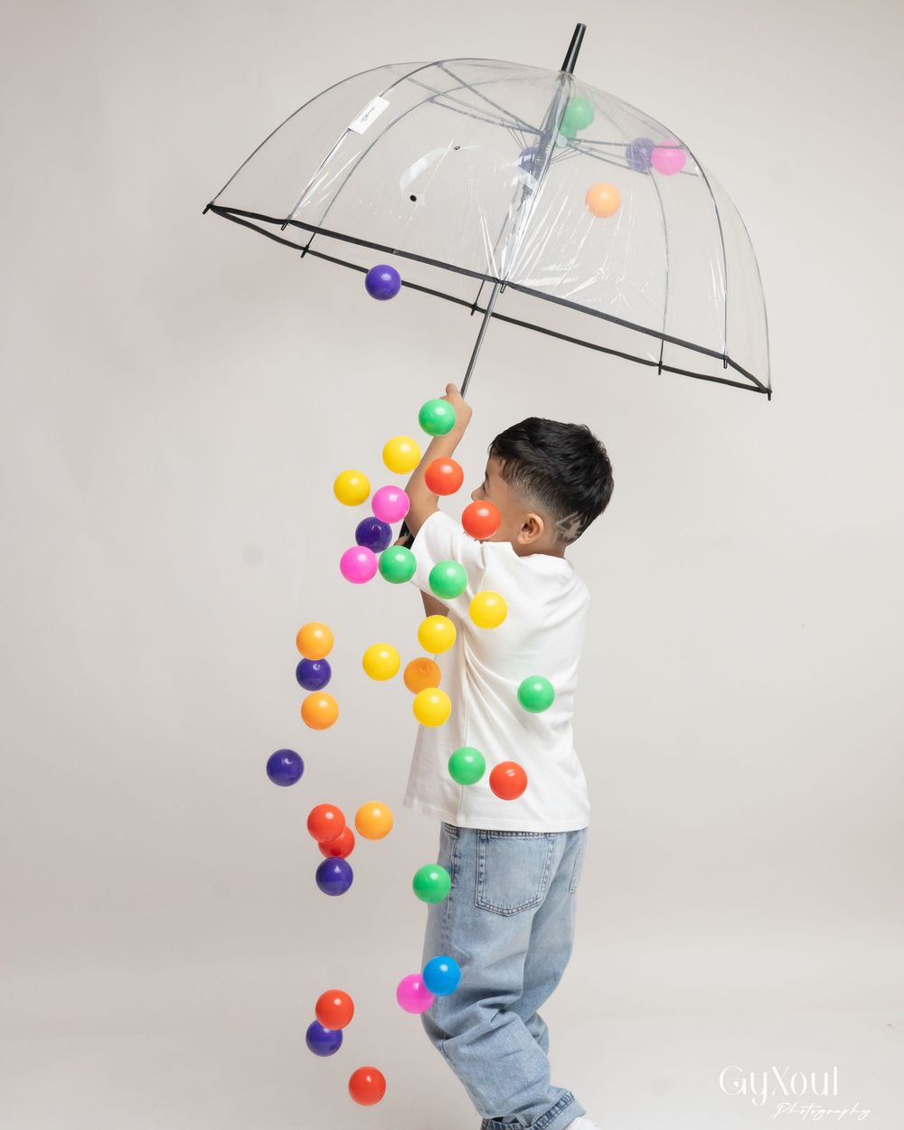 A clear umbrella with colorful floating balls creates a whimsical scene against a neutral background.