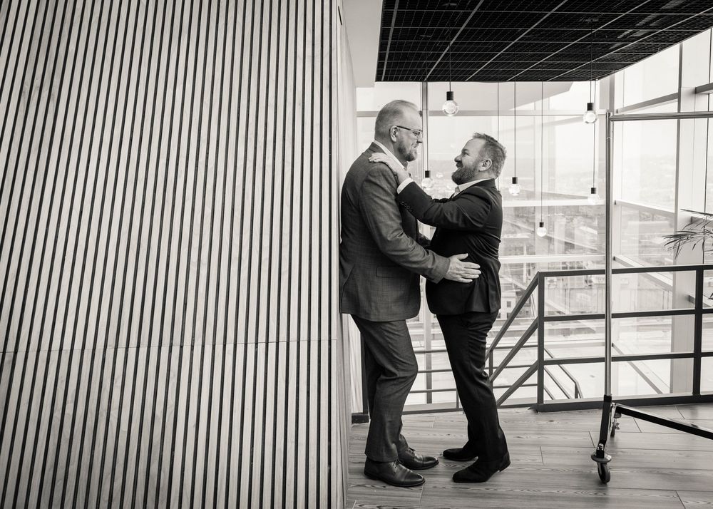 Two men in suits embrace and smile at each other in a modern building interior, black and white photo.