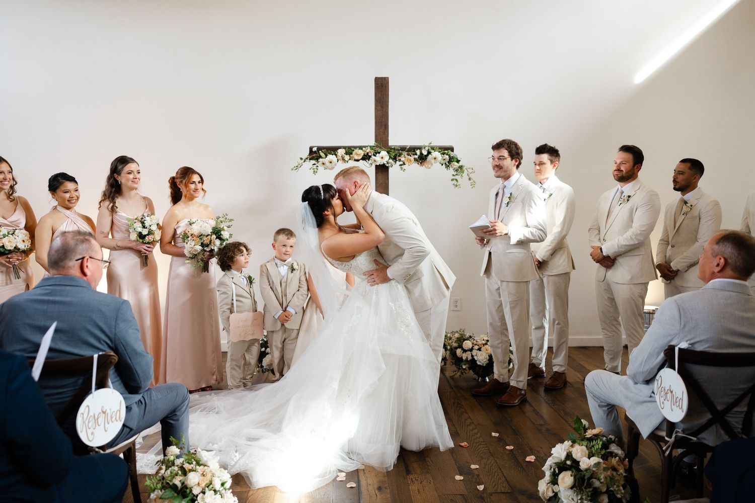 Wedding party members dance and celebrate during reception in elegant white and neutral toned venue.
