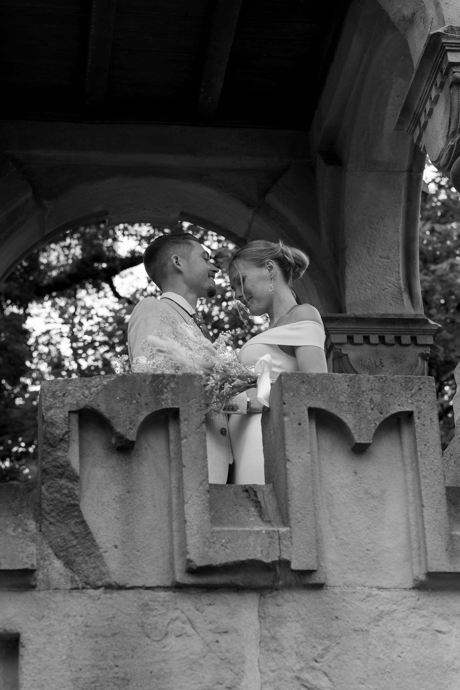 Eine romantische Schwarz-Weiß-Fotografie eines Paares, das einen intimen Moment auf einem Steinbalkon genießt.
