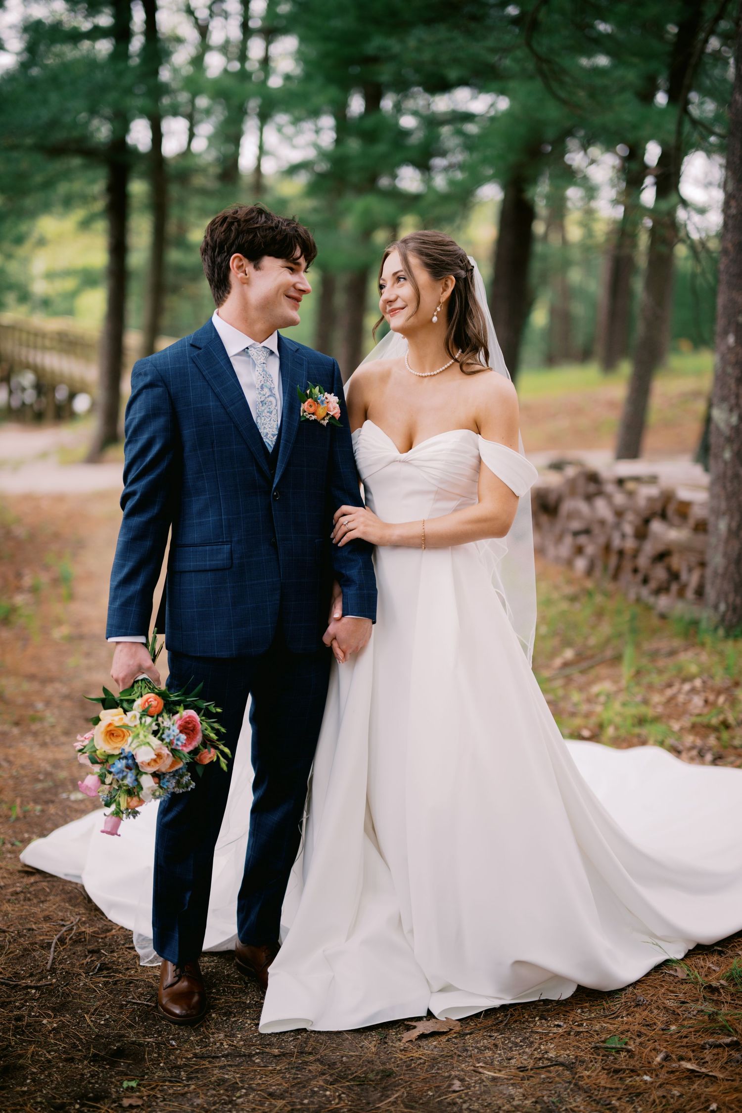 A romantic wedding couple walks through a pine forest while the bride's white dress flows elegantly behind them.
