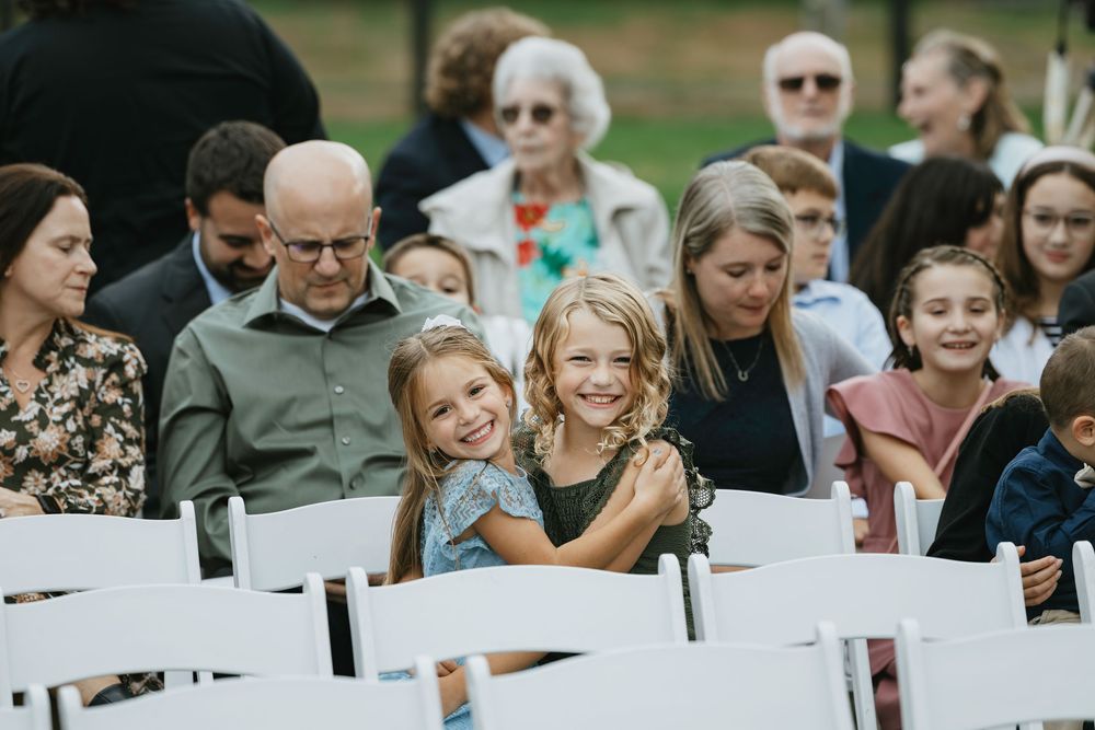 Wedding guests seated in white chairs on a lawn during an outdoor ceremony.