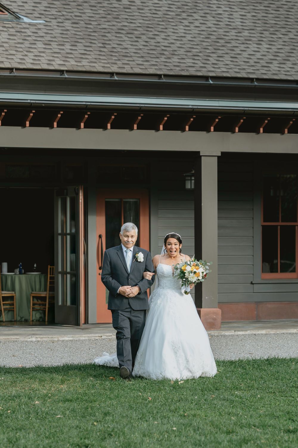 Outdoor wedding ceremony processional along a gray building with a white porch.