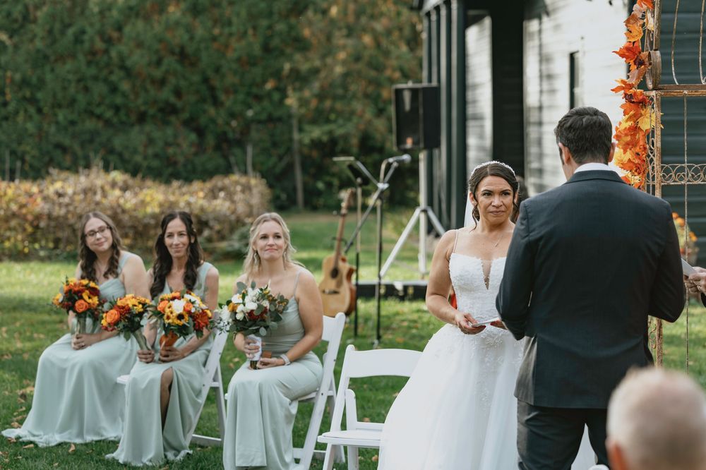 Wedding ceremony in progress under autumn foliage with bridesmaids in light blue dresses.