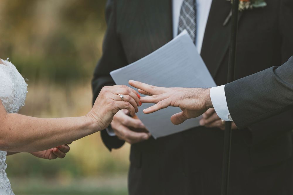 A close-up shot of hands exchanging wedding rings during an outdoor ceremony.