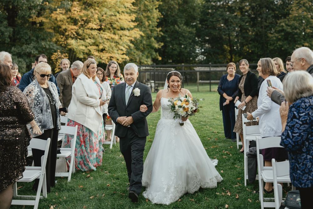 Outdoor garden wedding ceremony with white chairs arranged on a green lawn during a sunny autumn day.