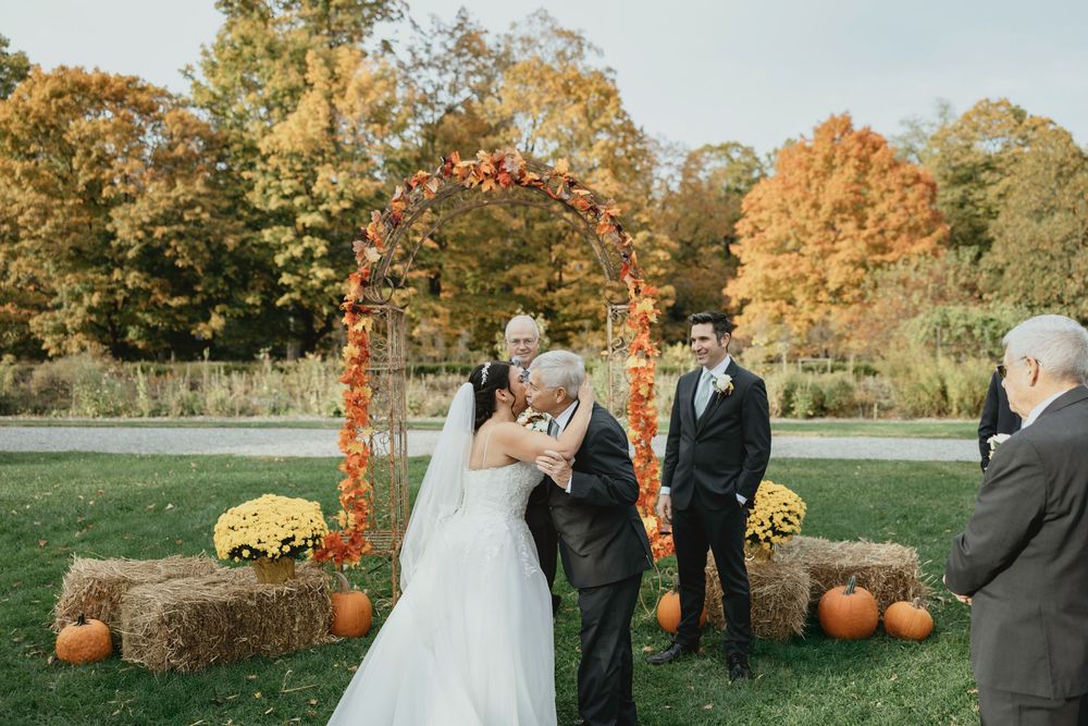 Outdoor autumn wedding ceremony with pumpkin decorations and fall foliage in the background.