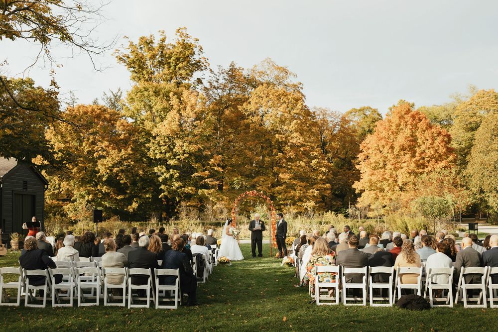 White chairs arranged in rows for an outdoor autumn wedding ceremony with golden trees in the background.