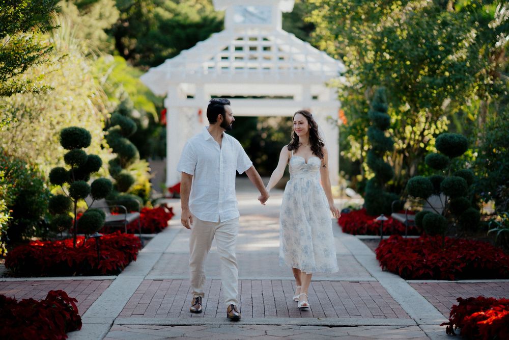 Couple dances together on an outdoor wooden deck with a white gazebo and red flowers in the background.