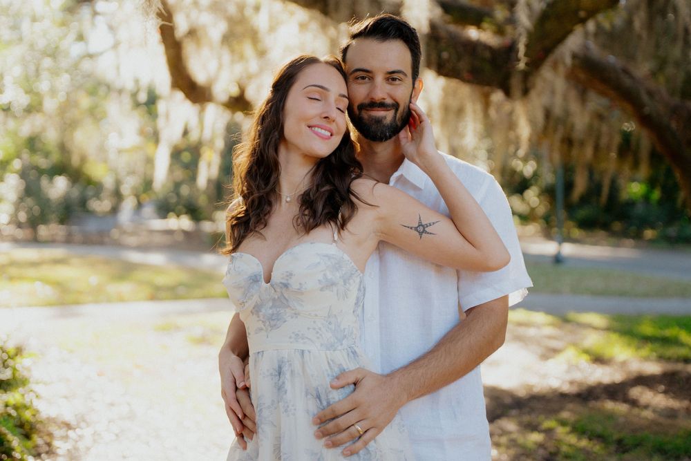 A couple embraces outdoors in a romantic photoshoot among sunlit trees and natural scenery.