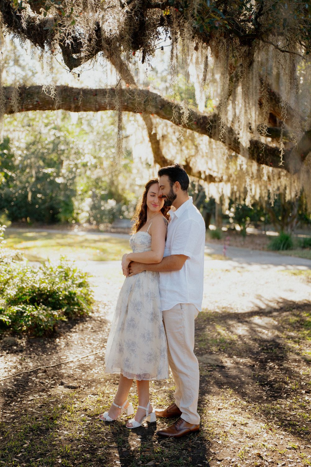 A couple shares tender moments under Spanish moss draped trees in a romantic outdoor setting.