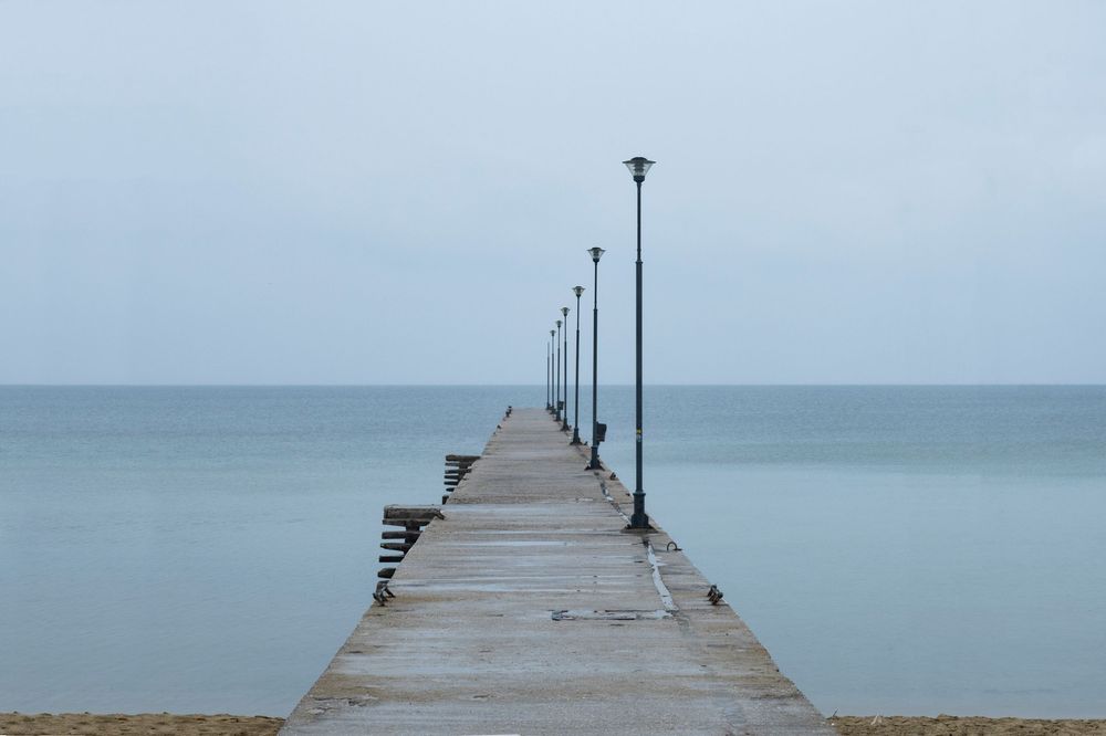 A long wooden pier extends into calm blue waters under an overcast sky.