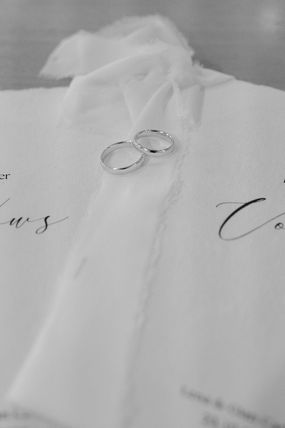Close-up of silver wedding rings resting on white fabric with handwritten text in the background.